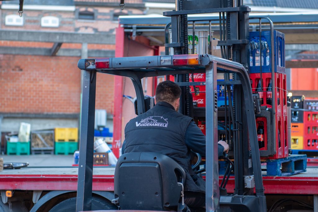 Een medewerker van Dranken Vandenameele laadt drankkratten voor levering aan een groothandelklant